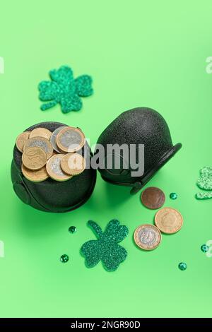 Pentole con monete, spicchi di carta e paillettes su sfondo verde. St Festa di Patrizio Foto Stock