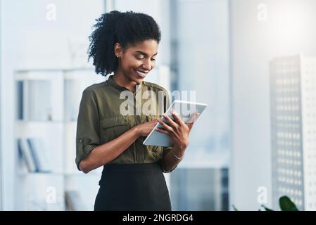 Ti tengono aggiornato su tutte le ultime tendenze. una giovane donna d'affari che usa il suo tablet digitale in ufficio. Foto Stock