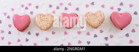 Amaretti dolci a forma di cuore e coriandoli colorati su sfondo bianco glitter. Biscotti alla francese con vaniglia, lampone e fragola. Banner pasticceria Foto Stock