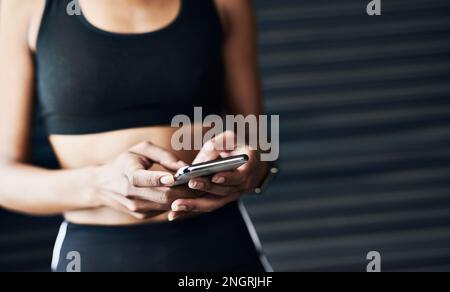 Tiene traccia dei suoi progressi sul suo cellulare. Primo piano di una donna sportiva con un cellulare su sfondo grigio. Foto Stock