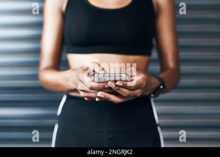 Ricerca sul Web di alcuni tutorial di allenamento. Primo piano di una donna sportiva con un cellulare su sfondo grigio. Foto Stock