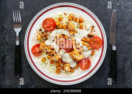 Burrito vegetale aperto con tortillas di farina, cavolo, cavolfiore arrosto, ceci arrosto e salsa piccante. Foto Stock