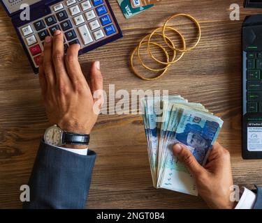 Mano di uomo di affari che si occupa di Ruppee pakistano banconote e oro per il bilancio risparmio di denaro di investimento e gestione contabile finanziaria o crescere Foto Stock