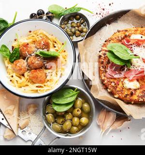 Tavolo completo di piatti italiani a bordo - pizza, pasta, polpette, salame, parmigiano, le olive, il pane si stacca su uno sfondo bianco. Vista dall'alto. Foto Stock