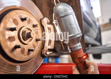 Un meccanico dell'auto ispeziona i dischi e le pastiglie dei freni con una torcia. Auto su un cavalletto di riparazione. Stazione di assistenza tecnica per auto. Foto Stock