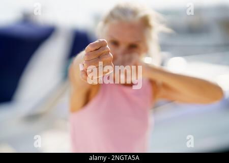 Donna più anziana che fa boxe ombra all'aperto. Donna anziana che fa sport in un porto costiero Foto Stock