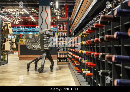 Carrello abbandonato vicino a scaffali di vino in un negozio di alimentari Foto Stock