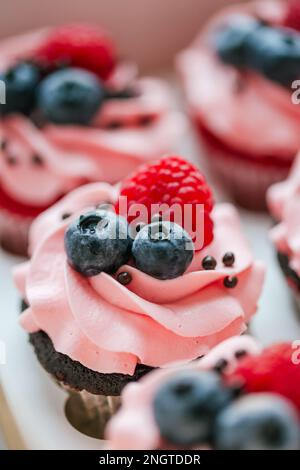 Cupcake freschi e deliziosi con crema di formaggio e frutti di bosco freschi. Vista dall'alto di gustosi cupcake disposti in scatola di cartone isolato su bianco. Torte con c Foto Stock