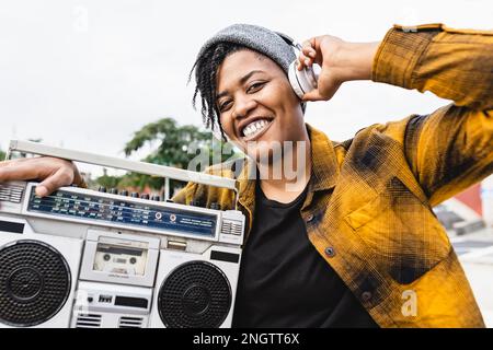 Felice ragazza africana che si diverte ad ascoltare musica con cuffie e stereo boombox vintage Foto Stock