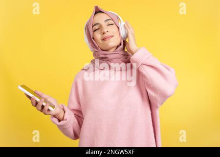 Donna musulmana rilassata che ascolta musica con il cellulare Foto Stock