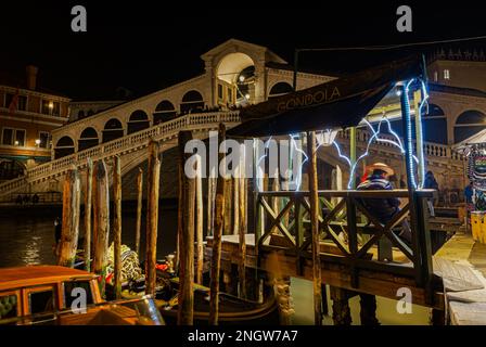 Vista notturna di Venezia sul Ponte di Rialto, Ponte pedonale di Rialto con gondoliere in fronte, accanto alle palazzine dei moli in legno. Foto Stock