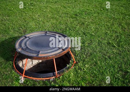 Aprire bene portello sul prato verde. Il coperchio del pozzetto d'ispezione è sul supporto. Dispositivo per la ventilazione di pozzi.. Foto Stock