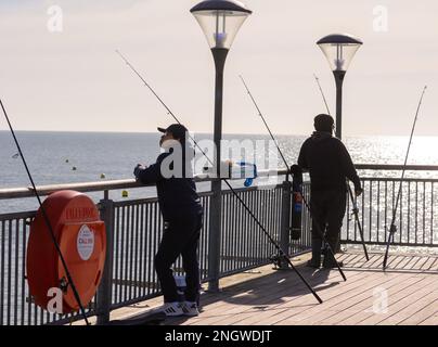 Boscombe, Bournemouth, Dorset, Regno Unito, 19th febbraio 2023, Meteo. La gente pesca fuori dal molo la domenica soleggiata come le temperature aumentano a 14 gradi nel sud dell'Inghilterra in caldo sole di fine inverno. Credit: Paul Biggins/Alamy Live News Foto Stock