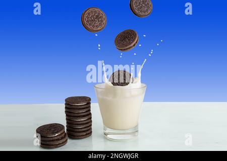 Un biscotto con scaglie di cioccolato cade in un bicchiere di latte. Foto Stock