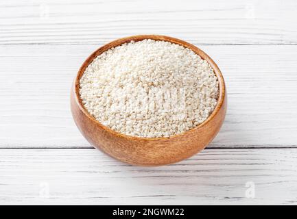 Semi di sesamo secchi in ciotola di legno su sfondo bianco di legno Foto Stock