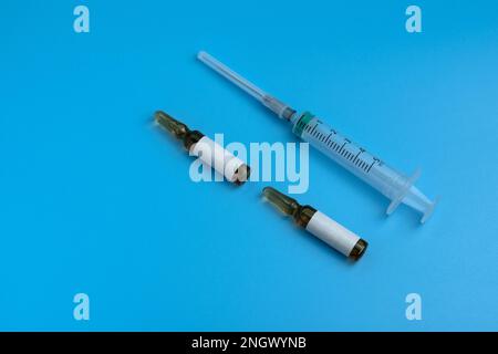 Una siringa per uso medico e due fiale sono isolate su sfondo blu. Fiale per preparazioni iniettabili. Sanità, medicina e concetto di vaccinazione. Foto Stock