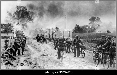 WW2 OPERAZIONE BARBAROSSA Una colonna di soldati tedeschi nazisti con biciclette entra in un villaggio sovietico sul fronte orientale che è già stato torcito dall'avanzare delle forze naziste. Data giugno 1941 Foto Stock