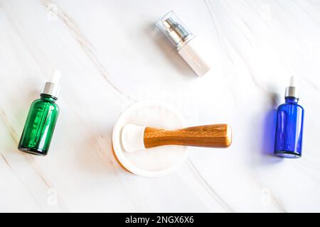 Contenitori per creme per la cura del viso, elessiri e oli essenziali su un tavolo in marmo con mortaio vuoto per erbe medicinali Foto Stock