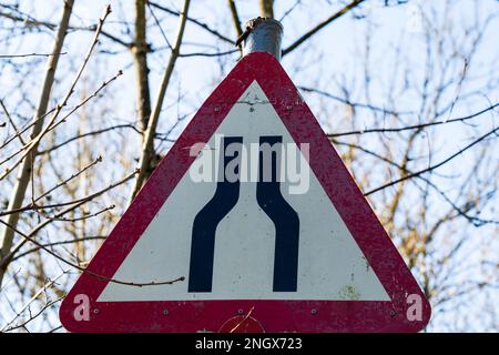 Cartello stradale del Regno Unito che indica che la strada si restringe davanti con un triangolo di segnalazione rosso e bianco Foto Stock