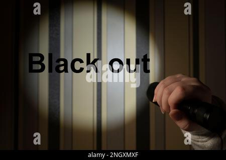 Umano in una stanza buia tiene una torcia portatile. La luce della torcia lascia un punto rotondo di luce sulla parete con l'iscrizione Blackout Foto Stock