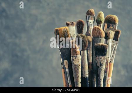 Pennelli usati su sfondo grigio. Un mazzo di spazzole per la verniciatura con vernici ad olio e acriliche. Pennelli per artisti in uno studio d'artista. Spazio di copia Foto Stock