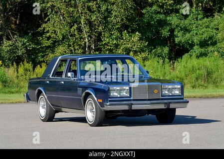 Un blu scuro 1982 Chrysler New Yorker Fifth Avenue Edition vista frontale contro gli alberi in sole luminoso. Foto Stock