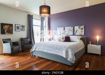 Letto king size con copriletto bianco nella camera da letto principale al piano superiore con poltrone in pelle grigia e pavimenti in legno Qumaru all'interno di una lussuosa casa moderna. Foto Stock