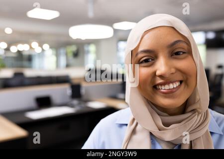 Felice mediorientale donna d'affari in hijab guardando la fotocamera in ufficio Foto Stock