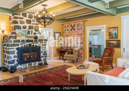 Divano letto in velluto rosso, poltrone imbottite in legno, tavolino in legno dipinto di bianco, caminetto a gas in pietra naturale nel soggiorno di 1920s casa. Foto Stock