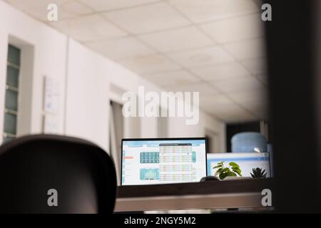 Ritratto di computer portatile con schermo acceso con software finanziario collocato su un tavolo da lavoro moderno con sfondo sfocato. Vista dall'angolo basso della stazione di lavoro vuota di notte. Foto Stock