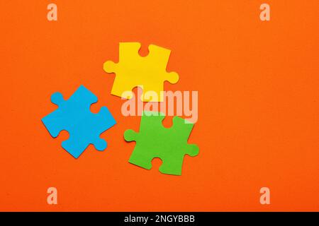 Tre pezzi di puzzle colorati blu, verde e giallo su sfondo arancione - Teamwork Concept Foto Stock