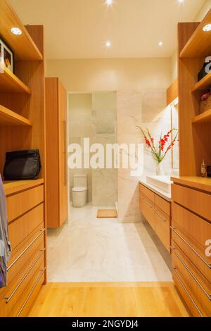 armadio a muro in legno Douglas abete con ripiano in marmo bianco e lavabo rettangolare in bagno con pavimento in marmo e pareti in condominio. Foto Stock