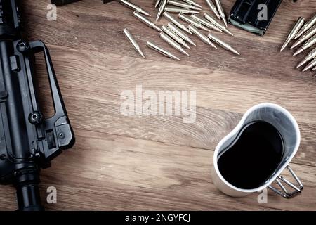 Fucile nero e caffè nero. Fucile d'assalto e tazza di caffè su sfondo tavolo di legno. Foto Stock