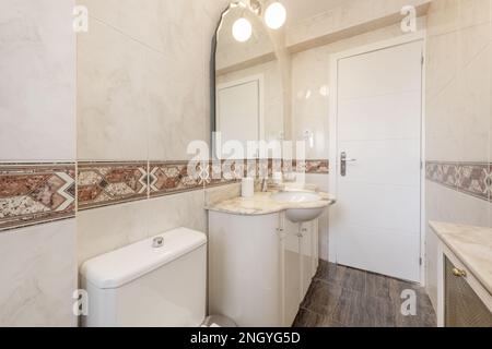 Bagno in stile ornato con mobili laccati bianchi con ripiano in marmo crema, specchio smussato sulla parete e bordo centrale sulle piastrelle Foto Stock