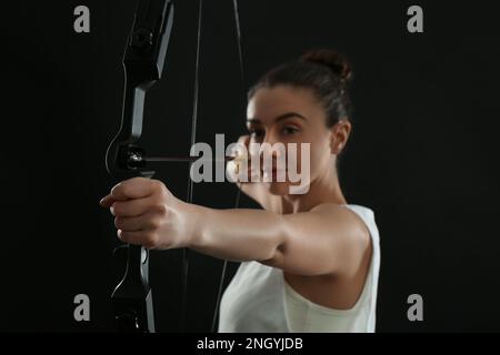 Donna con arco e freccia pratica tiro con l'arco su sfondo nero, fuoco a portata di mano Foto Stock