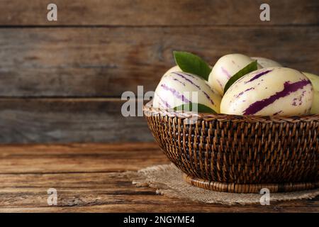 Meloni di pepino freschi e maturi con foglie verdi in cesto di vimini su tavolo di legno, spazio per testo Foto Stock