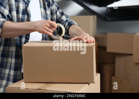 Uomo che nastrano scatola di cartone all'interno, primo piano. Giorno in movimento Foto Stock