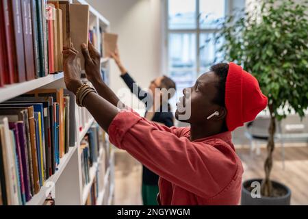 Messo a fuoco perplesso sull'individuazione dello studente di letteratura educativa di destra guarda attraverso le librerie in biblioteca Foto Stock