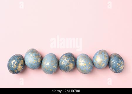 Uova di Pasqua blu e oro in fila su sfondo pastello rosa Pasqua, biglietto d'auguri, spazio copia, piatto, Foto Stock