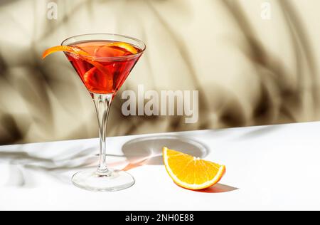 Cocktail Martinez con vermouth rosso, liquore, arancio amaro, scorza e ghiaccio. Sfondo beige chiaro, luce dura, motivo ombra Foto Stock