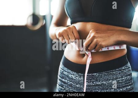 La prova è espressa in pollici. una giovane donna in forma che misura la vita in palestra. Foto Stock