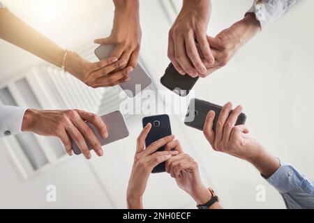 I team intelligenti utilizzano la tecnologia intelligente. Un gruppo di foto a basso angolo di un gruppo di colleghi che utilizzano i loro smartphone in sincronia utilizzando il loro smartphone Foto Stock