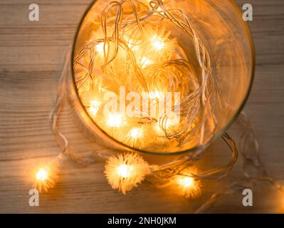 Vista dall'alto del vaso di vetro con ghirlanda luminosa dorata di Natale da lampadine a LED con soffice palla o punta in vaso di vetro su sfondo tavolo di legno. Top vie Foto Stock