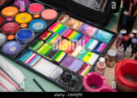 Scatole e tubi colorati con vernici su un tavolo. Vernici e pennelli per il make-up, per la pittura su volti, la pittura su volti, la pittura su volti Sfondo astratto Foto Stock