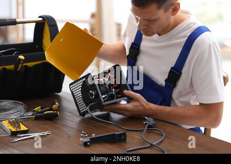 Tecnico professionista che ripara il riscaldatore della ventola elettrica al tavolo all'interno Foto Stock