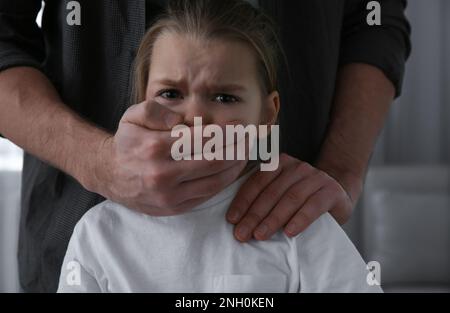 L'uomo che copre la bocca della bambina spaventa all'interno. Violenza domestica Foto Stock