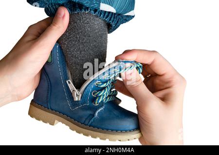 La madre mette delle scarpe blu sul bambino bambino del bambino del piede che siede nel corridoio domestico, isolato su uno sfondo bianco. Donna mamma vestirsi caldo stivali panno Foto Stock