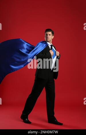 Uomo d'affari in capo supereroe che prende il vestito su sfondo rosso Foto Stock