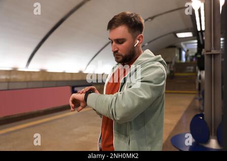 Giovane uomo con auricolari in attesa di treno alla stazione della metropolitana. Trasporti pubblici Foto Stock