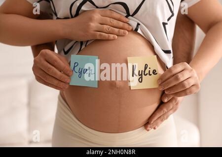 Uomo e donna incinta con diversi nomi di bambino sul ventre al chiuso, primo piano Foto Stock